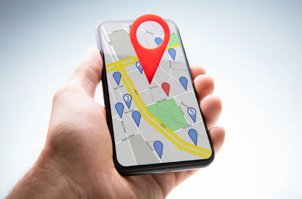 dłoń trzymająca smartfon z mapą, duża czerwona pinezka oznaczająca lokalizację
