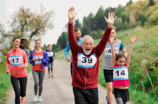 grupa biegaczy uśmiechnięty starszy pan finiszuje z rękoma w górze