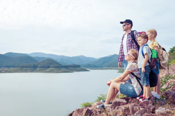rodzina w wycieczce w górach, rodzice i dwoje dzieci podziwiają widok ze szczytu, w tle jezioro